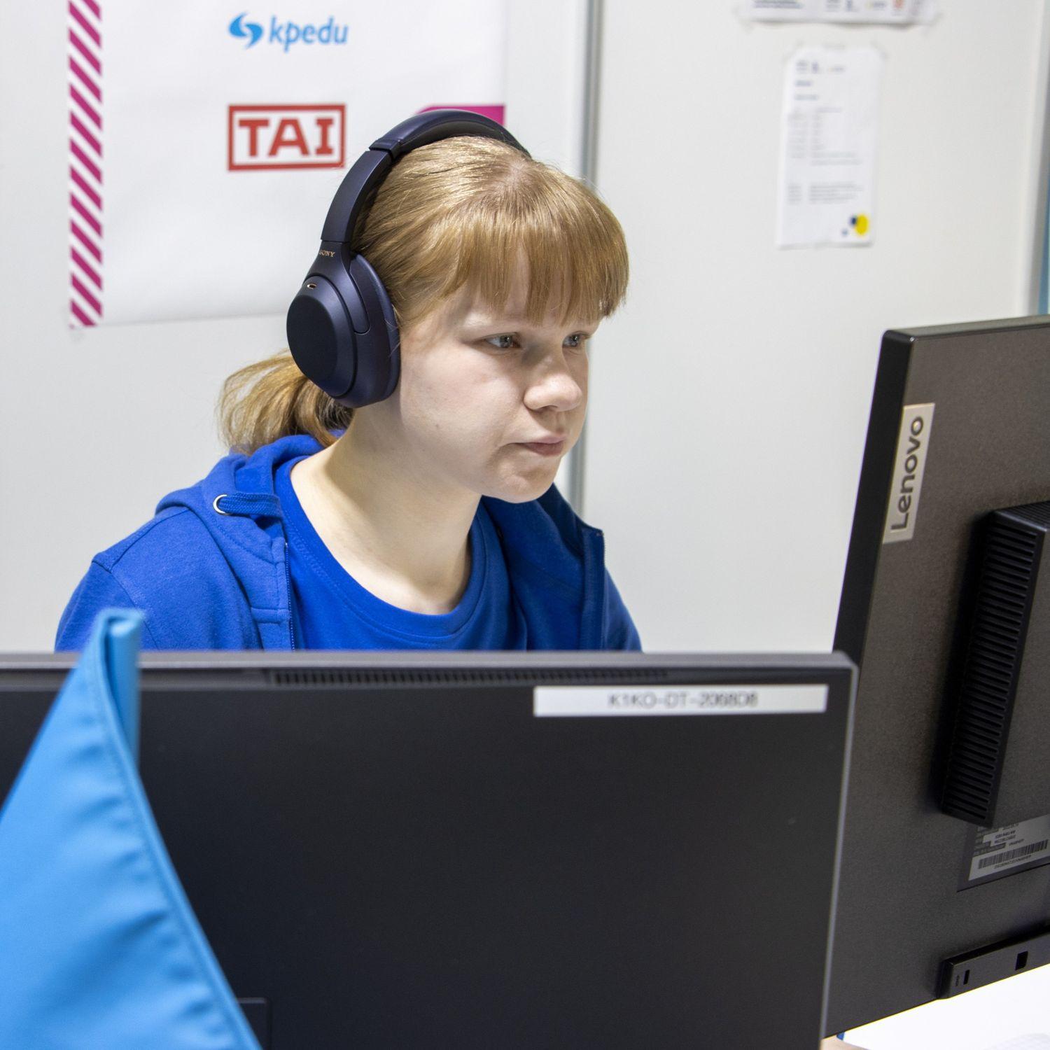 A competitor sits at a computer wearing headphones, with Taitaja event signage in the background.