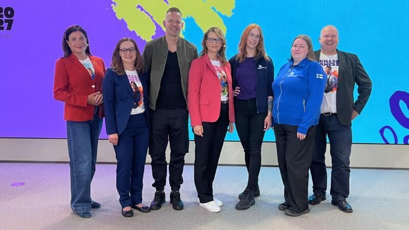 Skills Games 2027 -avauslähetyksen puhujia ja järjestäjiä yhteiskuvassa tapahtuman värikkään taustan edessä.